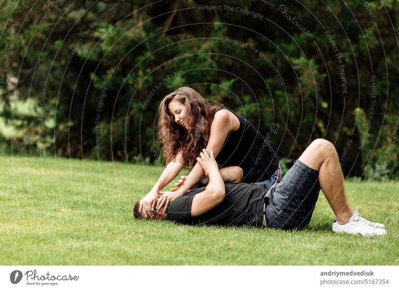 young couple is having fun and playing on the grass on summer day. woman lying over her lover, smiling park cute sunny lifestyle green nature leisure happy