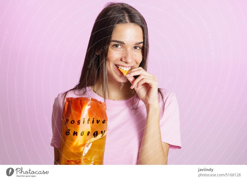 Woman eating tasty crisps pink background woman smile positive energy nacho chips enjoy snack treat colorful vibe optimist delicious cheerful yummy young female
