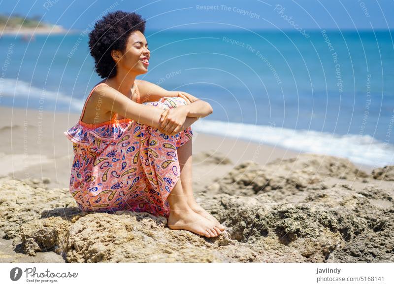 Happy African American woman spending time on beach traveler sea relax summer happy stone vacation wave female black african american ethnic embracing knee