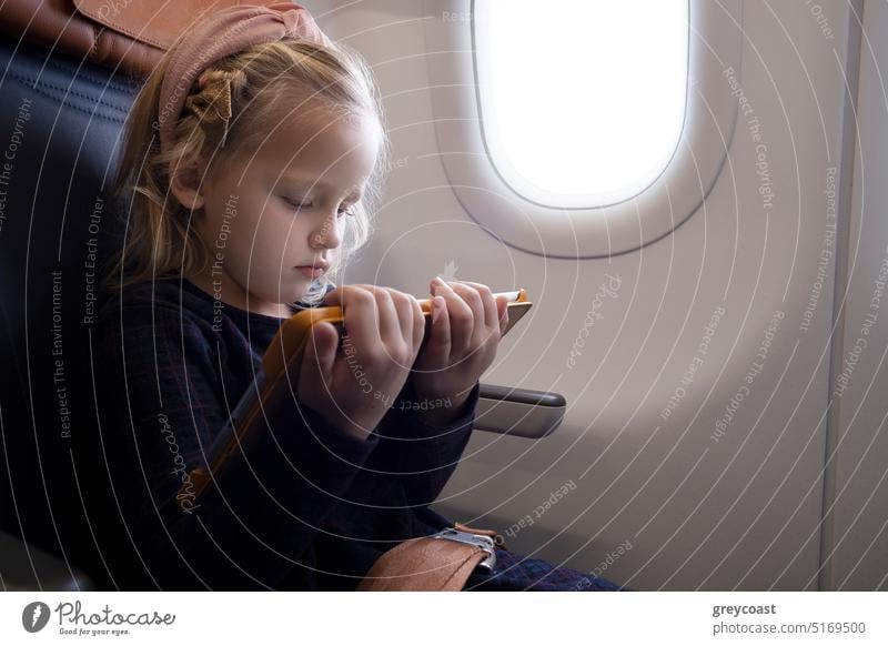 Focused girl watching video on tablet in plane child kid concentrate using airplane passenger gadget cartoon browsing internet seat device preteen online sit