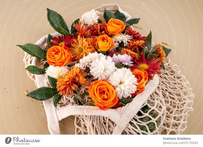 Orange and red garden flowers in the mesh bag Mockup white tags with space for text Background in natural earth tones Roses, daisies, chrysanthemums mothers day