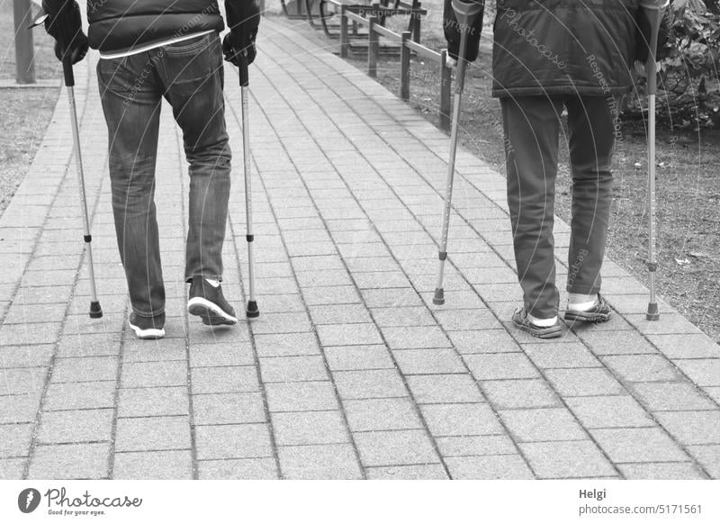 Back view of two men walking with forearm crutches Human being Man Senior citizen Rear view partial view Legs props Going Walking Park off Health resort