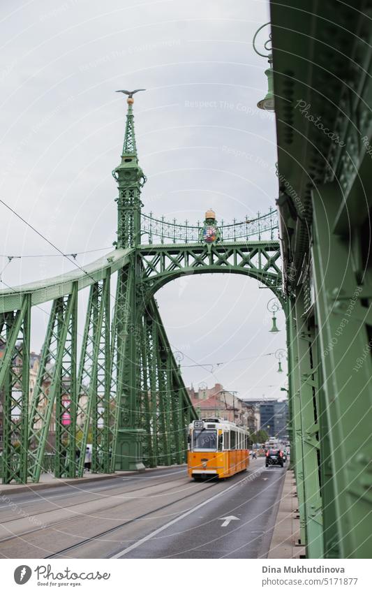 Yellow tram riding through famous green Liberty Bridge in Budapest, Hungary. Historic landmark. bridge tramway tourism budapest liberty transportation landscape