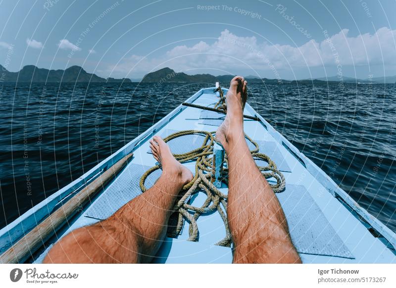 Legs of man on banca boat approaching tropical island. travel, summer exotic vacation holidays concept tourist relaxation personal perspective happy relaxing