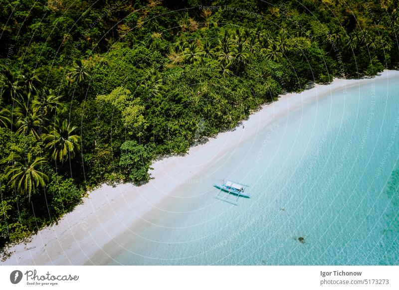 Aerial drone view of a beautiful secluded deserted tropical beach. Lonely boat in turquoise lagoon in front of rainforest jungle. Cadlao Island, El Nido, Palawan