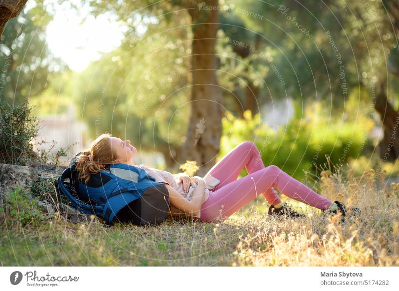Young woman hiking in countryside. Girl is lying under the tree and having rest and relax. Concepts of adventure, extreme survival, orienteering. Single travel. Backpacking