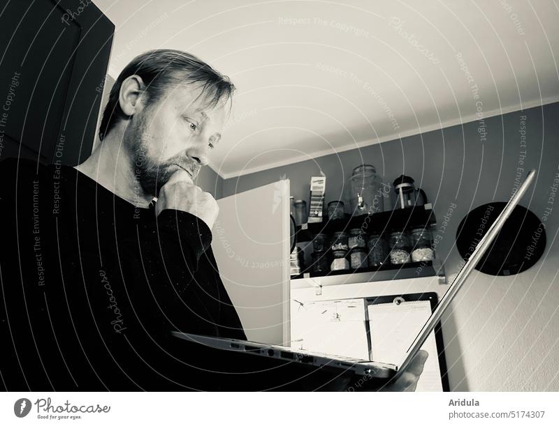 Thoughtful man working standing in kitchen with laptop in hand in b&w Man Kitchen Meditative home office Improvisation labour Notebook Online Computer Workplace