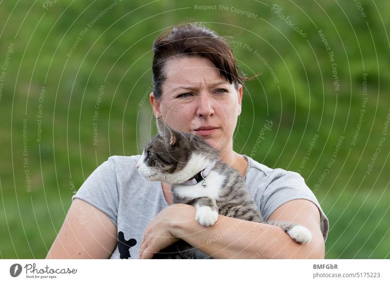Woman holding cat in her arms. Woman looks critically to the right, cat critically to the left. Cat stop Poor different Directions Right Left Funny cute Green