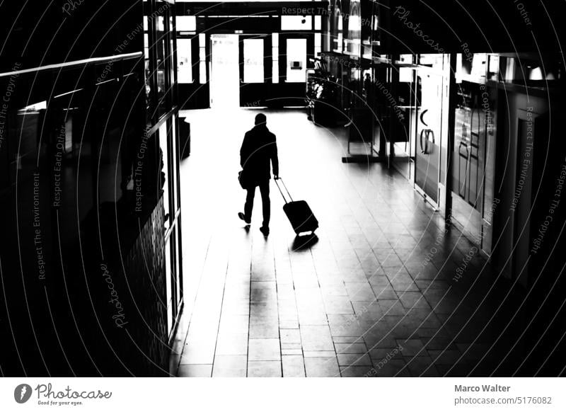 A silhouette of a man with rolling suitcase in a train station concourse Black & white photo Silhouette Station hall Train station Suitcase trolley Man travel