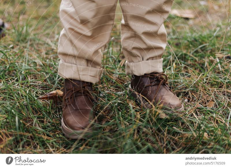 Cropped photo of kids legs in leather brown shoes and beige pants outdoors at autumn park with maple leaves Children adventure on fresh air. International Children's day