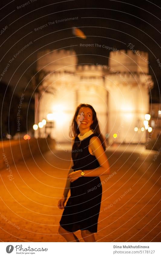 Happy woman walking at night in European town in front of a illuminated castle, smiling. Happy woman walking in the historic center of the city with lights. Smiling happily, going to the party. Young and beautiful female tourist in Spain.
