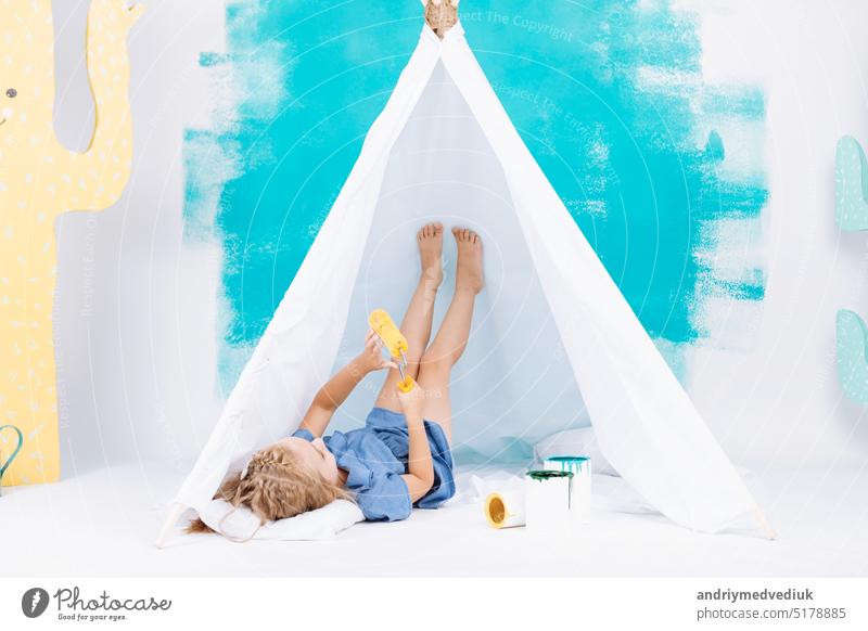 Portrait of a beautiful smiling girl with a paint roller. Little girl playing in a white wigwam on a background of colorful walls. Cheerful cute baby having fun in the nursery. baby's day.