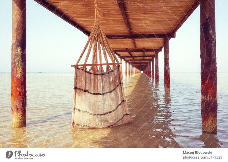 Hand woven natural fiber hammock under a pier, selective focus, color toning applied. beach vacation water sea holiday relax outdoors ocean getaway toned retro