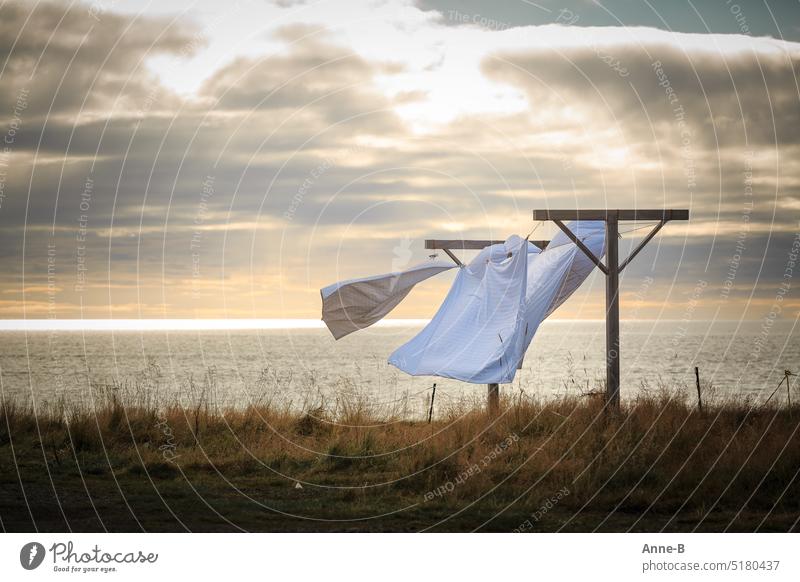 White bed linen waving in the wind on a meadow next to the sea in wonderful backlight and slightly cloudy sky. Laundry leash out dries Wind Weather Sea Wind