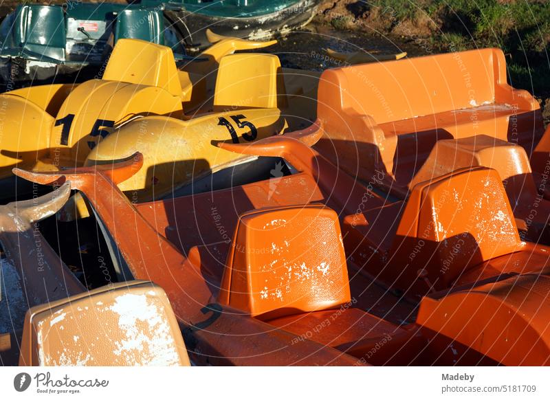 Old plastic pedal boats in bright yellow and orange in dolphin design at the jetty in summer in the light of the evening sun at Poyrazlar Gölü near Adapazari in Sakarya province, Turkey