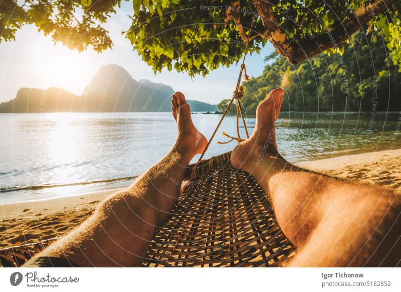 Feet of adult man relaxing in a hammock on the beach during summer holiday feet asia rest romantic sand sea serenity shade shadow sun swing thailand traditional