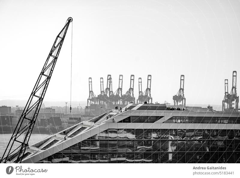 Side view of a part of the dockland with people on the stairs and the observation deck, in the background port cranes and containers, black and white, horizontal