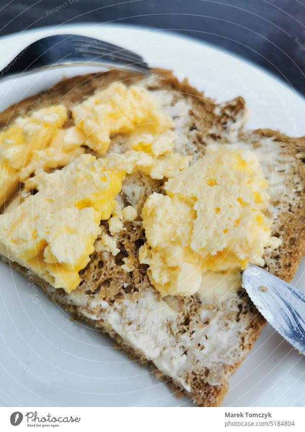 Buttered bread with scrambled eggs on a plate with a knife and fork. Bread and butter Scrambled eggs Breakfast Dish Colour photo Filling Slice of bread Close-up