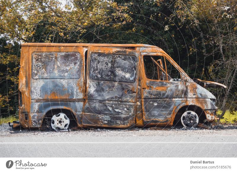 Burnt out big van next to the road. The car after the accident. A burnt-out car without windows and tires abandoned asphalt auto automobile blackened break down
