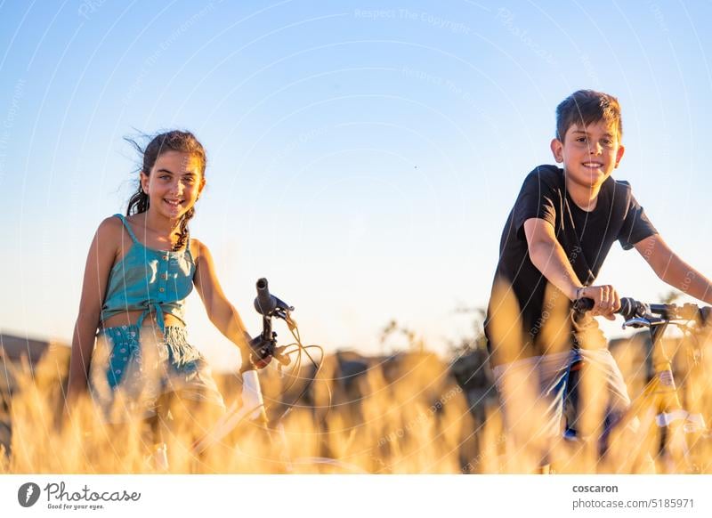 Two kids on a bike in front of a wheat field actions active adolescence adventure bicycle bicycling bicyclist biking boy child childhood country countryside