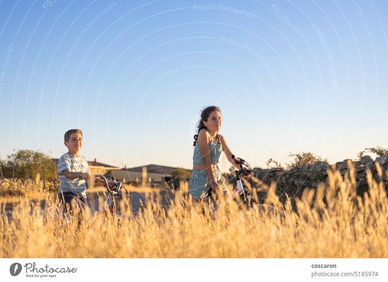 Two kids on a bike in front of a wheat field actions active adolescence adventure bicycle bicycling bicyclist biking boy child childhood country countryside
