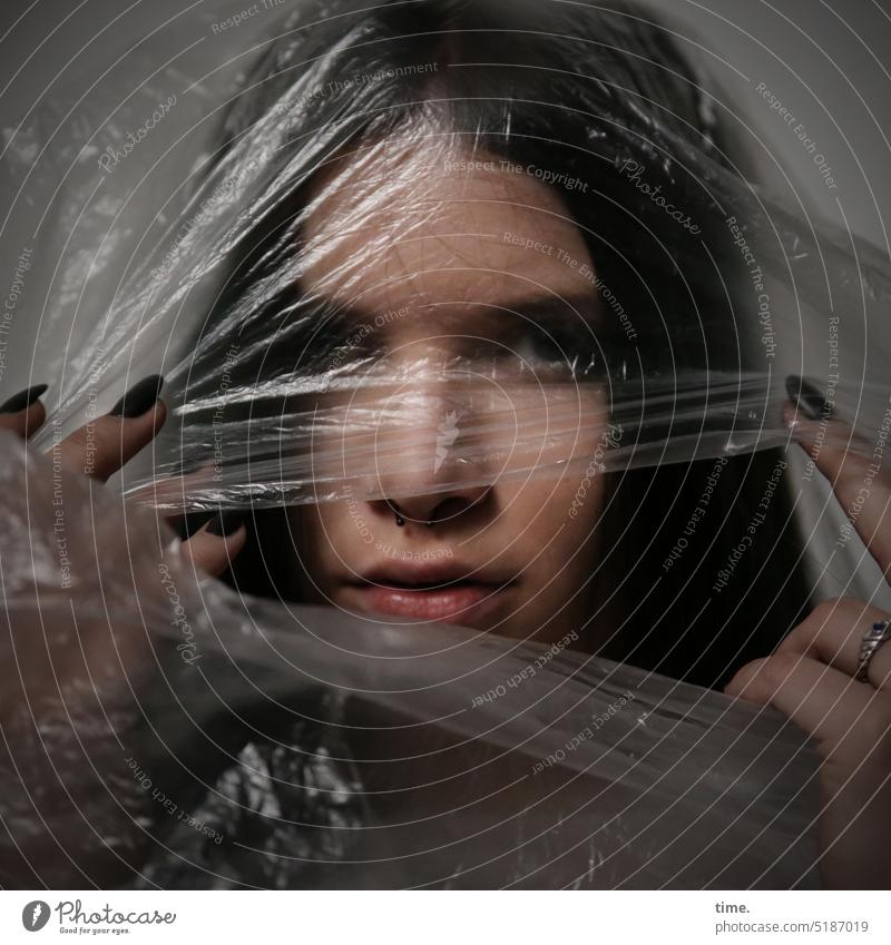 Woman with plastic wrap portrait Packing film plastic foil Dim Looking into the camera Protection Safety handle stop hands Fingers reflect shine wrinkled