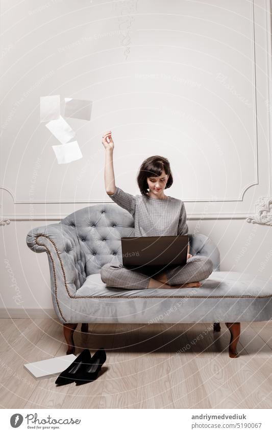 Beautiful businesswoman in gray suit is using laptop and scattering paper documents in a desire to take a break from work. High quality photo. mock up. selective focus.