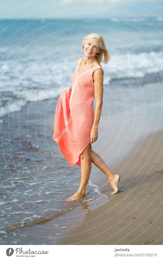 Mature woman on shore of a beach. Elderly female enjoying her retirement at a seaside retreat. mature senior old person lifestyle happy holiday relaxing sand