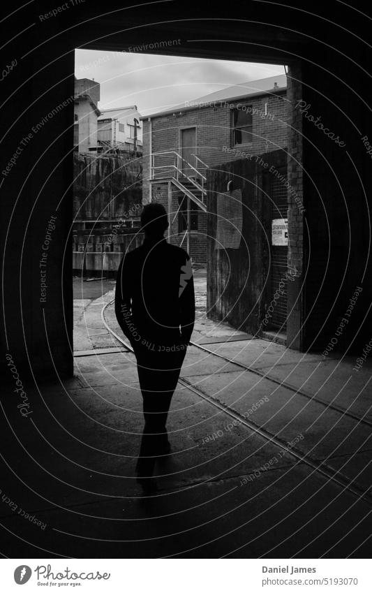 Dark figure strolls through industrial landscape Black & white photo silhouette people doorway Silhouette Exterior shot Shadow Contrast Deserted Railroad tracks