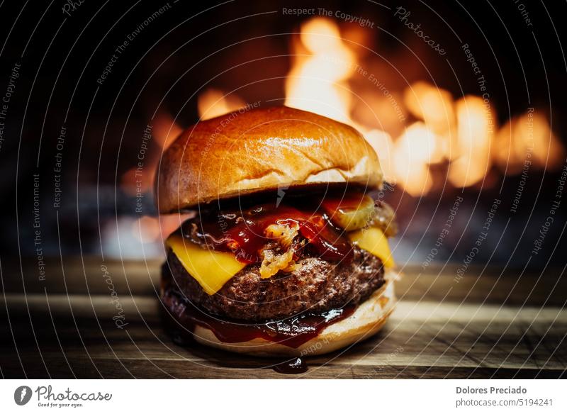 Cheeseburger on a wooden table in front of a fireplace. american background bacon barbecue barbequed bbq beef big bread bun caramelized cheese cheeseburger