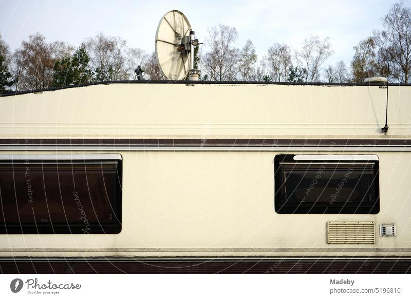 Caravan in beige and natural colors for camping and vanlife with satellite dish for TV reception on the campsite at the glider airfield in Oerlinghausen near Bielefeld on the Hermannsweg in the Teutoburg Forest in East Westphalia-Lippe.