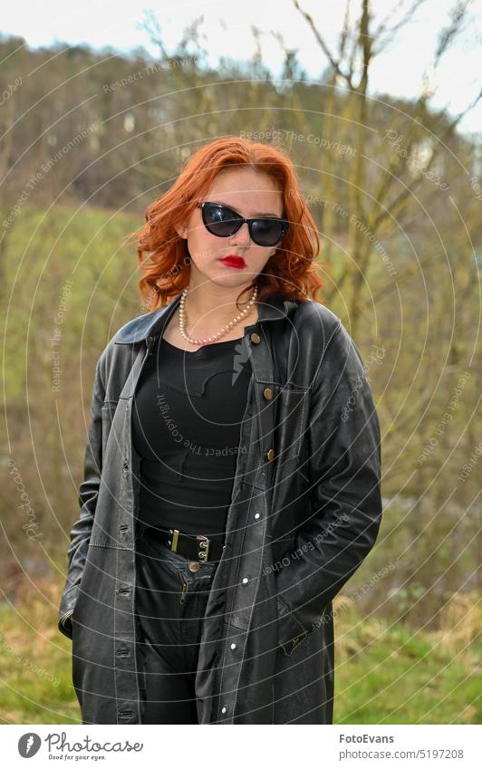 Young woman wearing black sunglasses standing with serious face in nature portrait joyless depressed grief youthful look red heartache outside real coat clothes