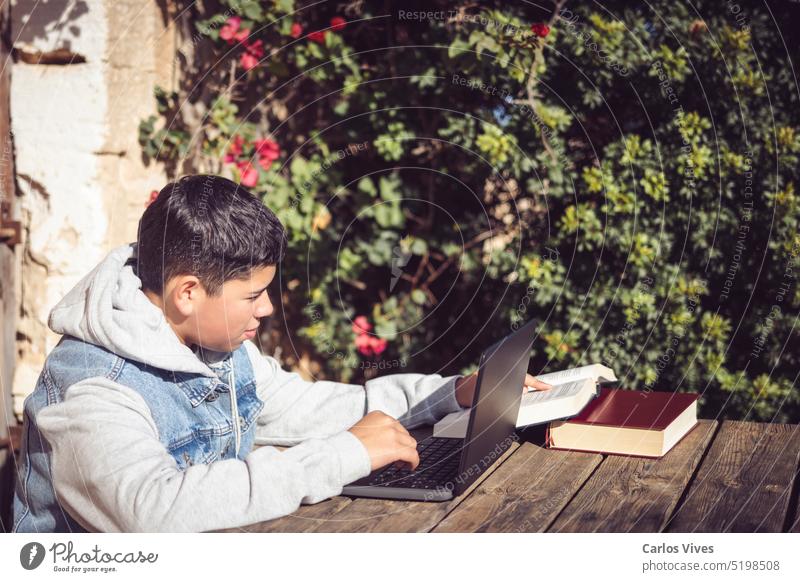young latin man reads book in front of laptop, outdoors books bookshelf boy centered close-up communication computer concentrated concentration concept