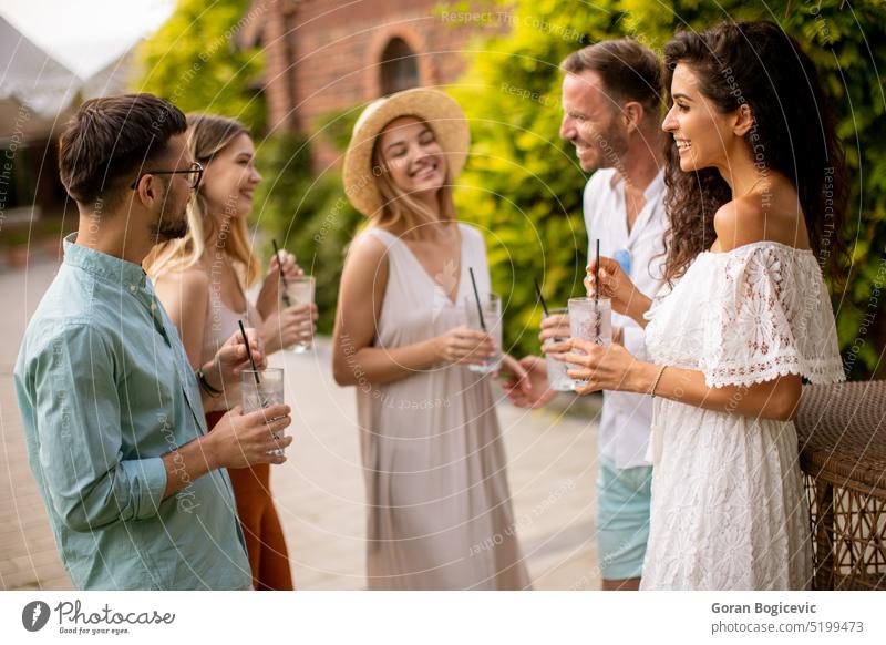 A group of young people gather outdoors to enjoy each other's company and refreshing glasses of lemonade standing drinking gathering socializing refreshment