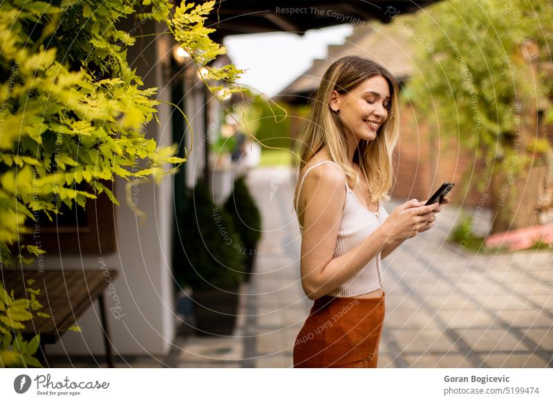 A young woman using her mobile phone in a garden on a beautiful summer day scenery distracted technology casual relaxed nature green outdoors enjoying leisure