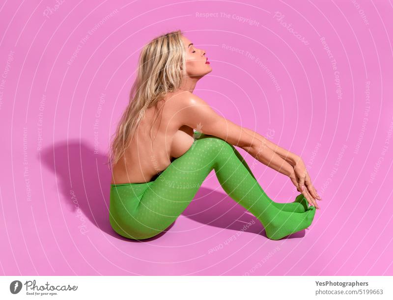 Fit woman with long blonde hair, in green tights and topless, minimalist on a purple background aging athletic beautiful body bright caucasian closed eyes color