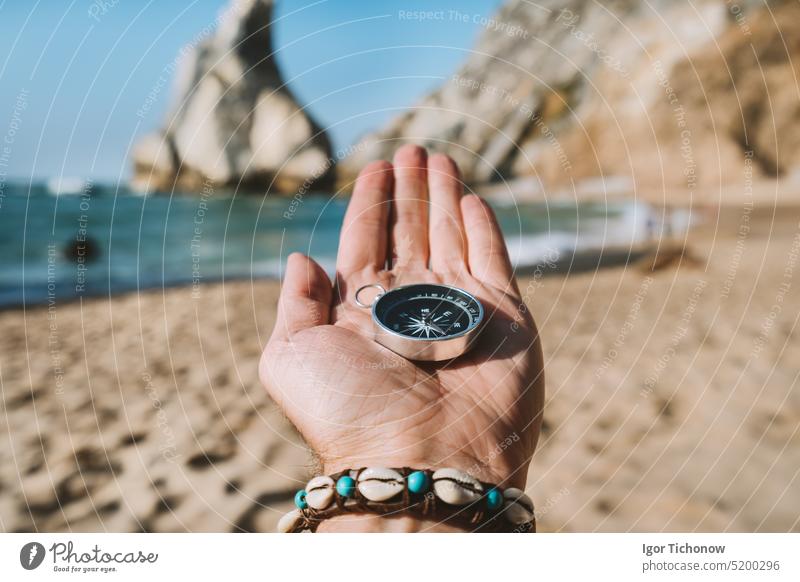 Man hand with compass symbolling adventure-seeking concept against Ursa beach, Sintra, Portugal travel holiday discovery sea lifestyle navigation traveler water