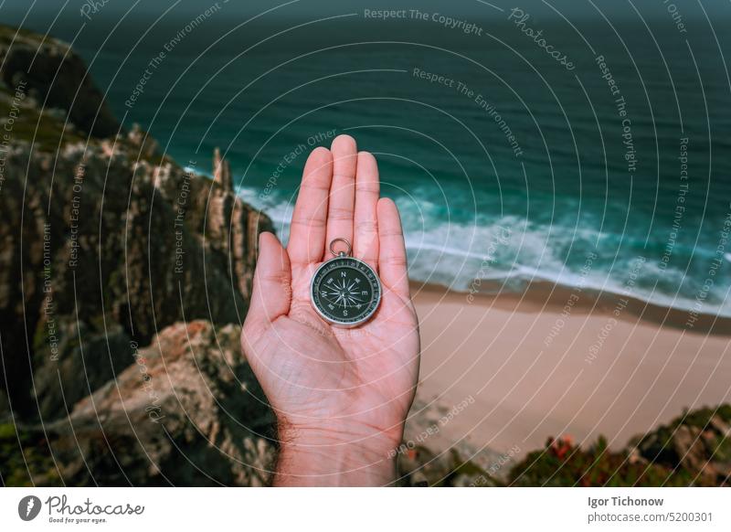 Looking at the compass in man hand palm symbolling adventure-seeking concept against sea and waves in coastline in background beach discovery lifestyle travel