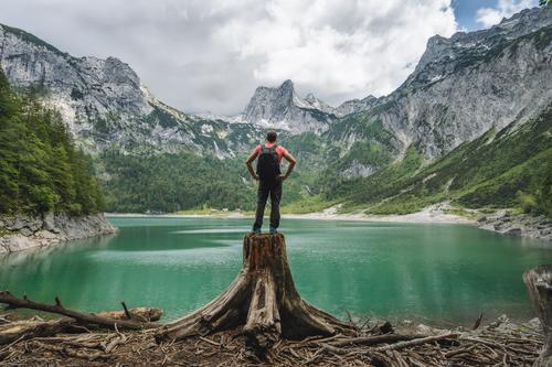 Man traveler standing on tree stump ejoying view of Dachstein peak mountains on a Upper Gosau Lake. Gosau, Salzkammergut, Austria, Europe gosau europe man