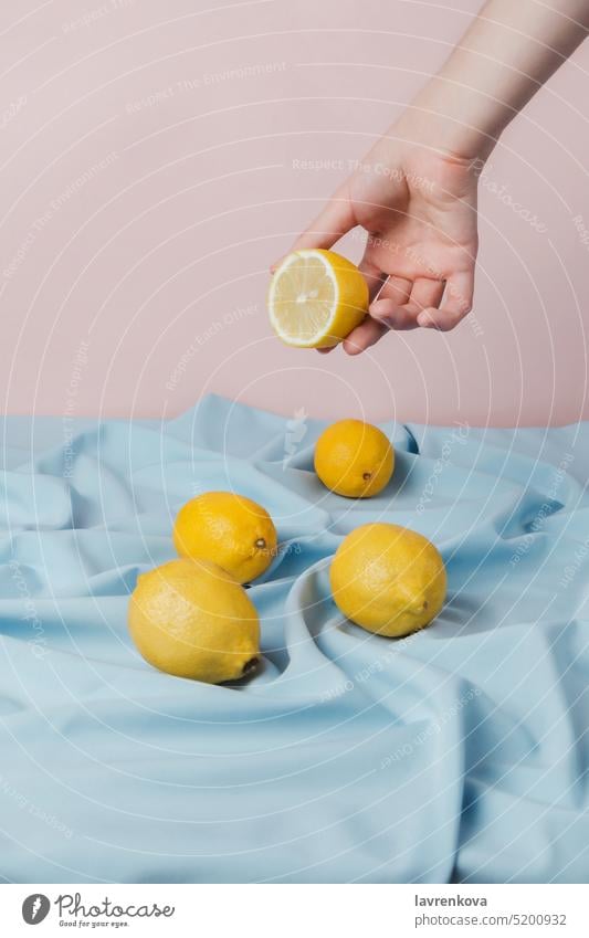 Female hand picking half of lemon from a table covered with blue drapery, fresh yellow fruit cut tasty sweet juicy citrus food ingredient tropical ripe vitamin