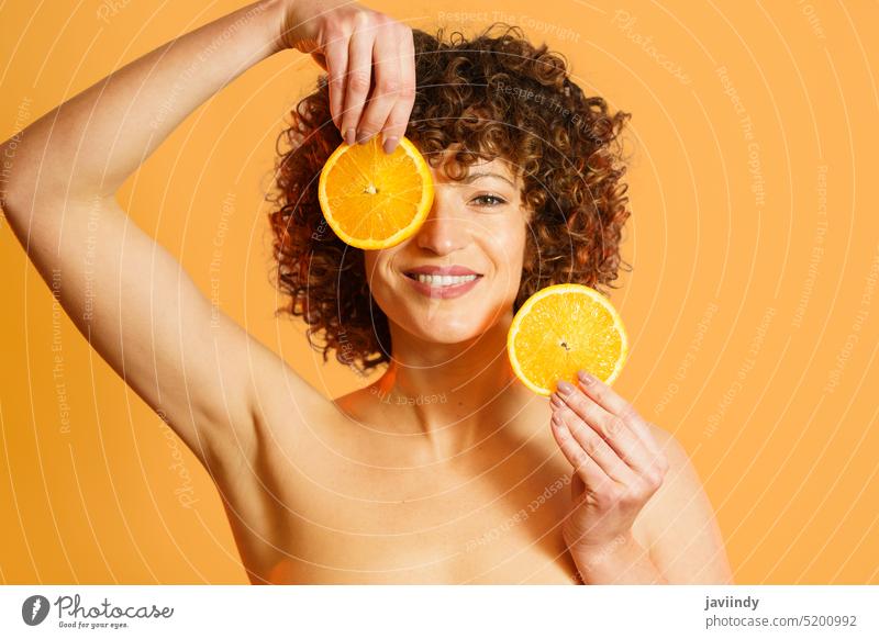 Cheerful female model with slices of orange woman smile skin care vitamin c cover eye spa bright color monochrome citrus fresh curly hair bare shoulders clean