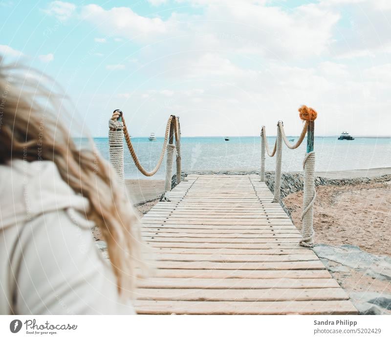 Girl with blonde hair leaves a footbridge leading to the sea Footbridge Ocean Water young woman blonde vacation Sky Vacation & Travel Beach Exterior shot Summer