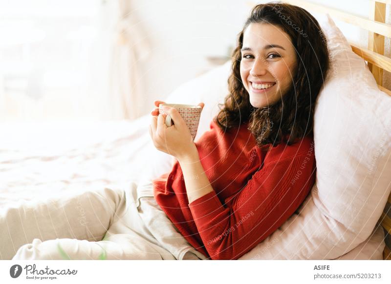 Happy woman having a coffee on the bed young cup drink tea smiling comfortable breakfast resting relax wellbeing enjoying bedroom cozy person indoor home mug