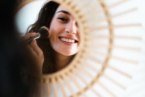 Young happy woman appying make up in front of a round mirror young brush cosmetic applying make-up smile smiling toothy powder blush face attractive girl