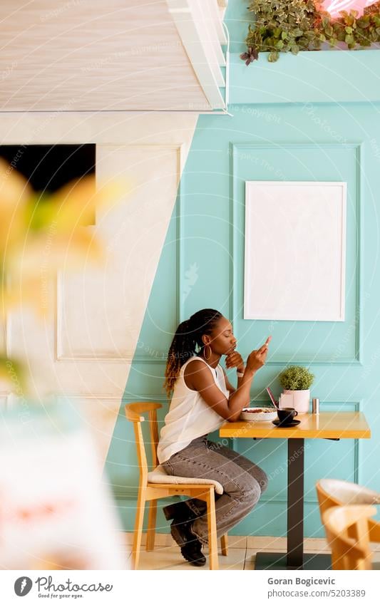Young black woman using mobile phone while having breakfast in the cafe female person young coffee lady afro beautiful casual cup shop lifestyle lunch happy