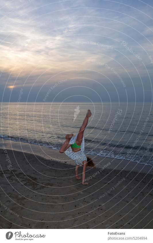 Girl in dress does handstand on beach in front of sea at sunset Child Dress Ocean Beach Sand Sandy beach Sunset Nature Landscape Handstand Sports active fun Joy