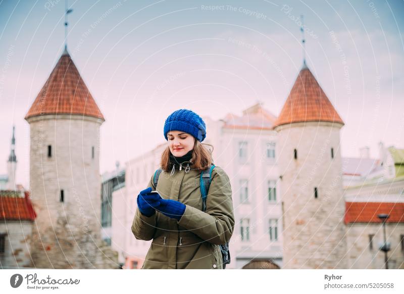 Tallinn, Estonia. Young Caucasian Confident Woman Backpacker Tourist Using Smartphone Near Landmark Viru Gate. Vacation In Old Town. Girl Surfing Net Internet In Phone
