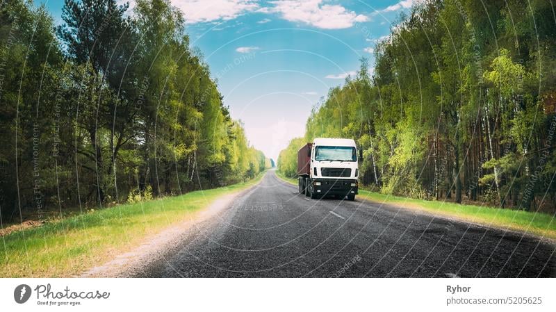 Truck, Tractor Unit, Prime Mover, Traction Unit In Motion On Country Road Through Forest, Freeway. Cloudy Sky Above Asphalt Motorway, Highway. Business Transportation