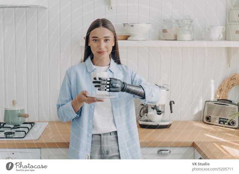 Disabled girl holding cup by bionic prosthetic arm in kitchen. Lifestyle of people with disabilities prosthesis disability grasp female cozy artificial coffee