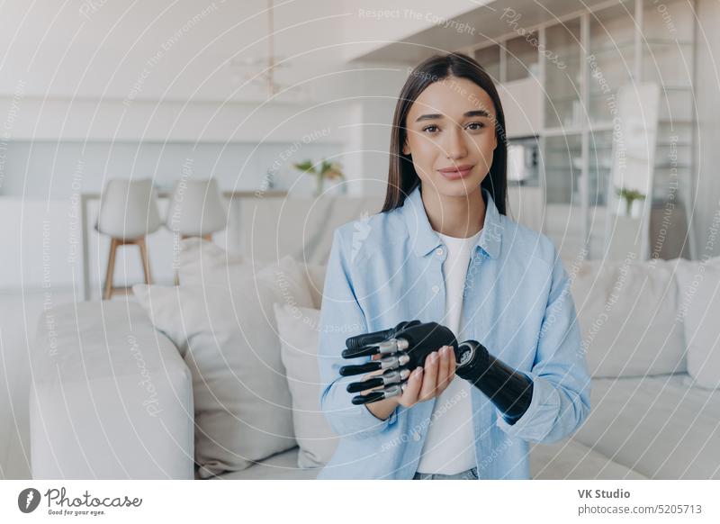Beautiful caucasian girl with disability taking apart her bionic prosthetic arm, standing at home. disabled prosthesis hand artificial limb hold healthcare